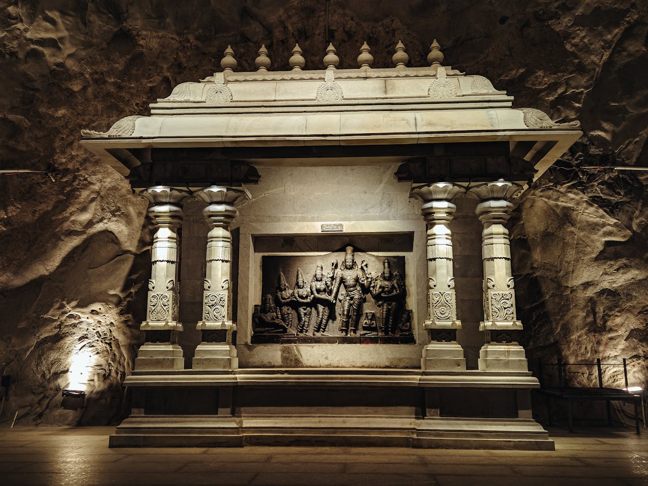 Anasayfa Detailed stone carving of deities in an ancient temple cave with intricate columns, dimly lit ambiance.
